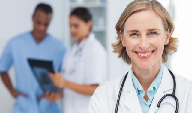 Practice management doctor in lab coat with stethoscope around neck smiling into the camera.
