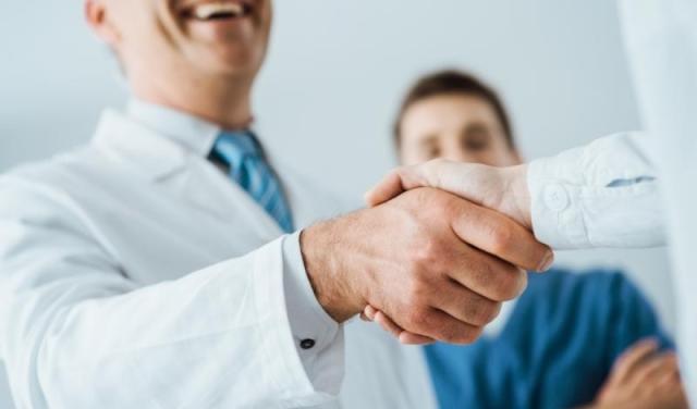 Firm handshake between two practice management doctors wearing white coats.