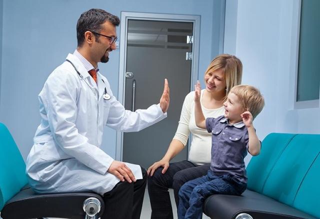 Doctor in lab coat celebrating workflow efficiencies with a young patient and his mom with a high five.