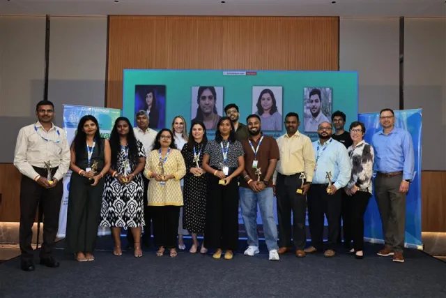 a group of Greenway India employees wearing badges holding trophies in a room with wood walls