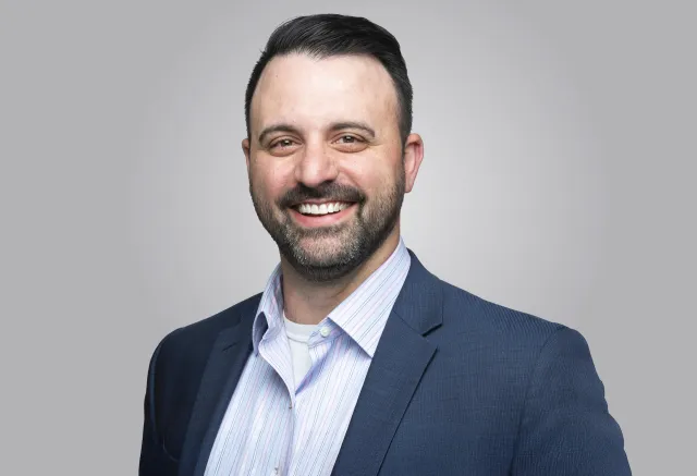 headshot of man smiling wearing a blue coat