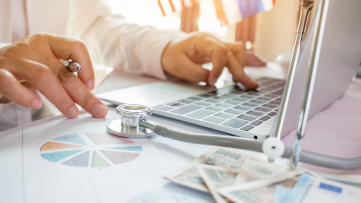 doctors hands typing on laptop with charts and graphs on table